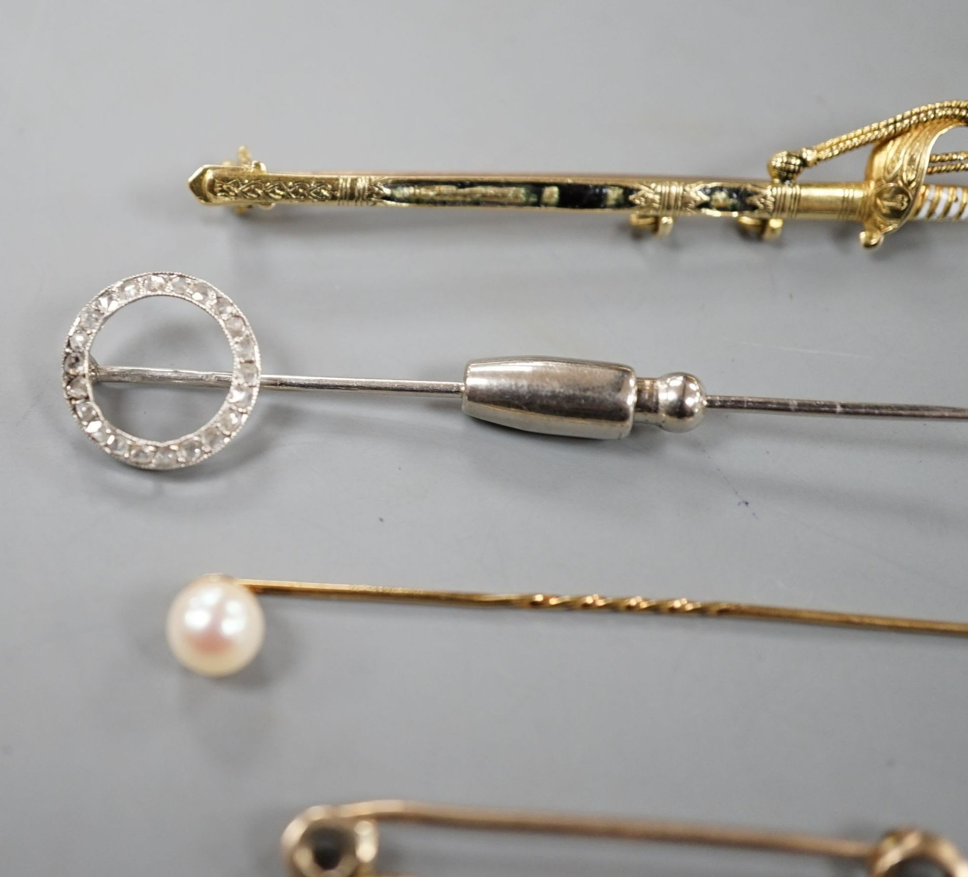 A French white metal (poincon mark for platinum) and diamond set tie pin, 64mm, gross 3.4 grams, a 15ct and enamel(a.f.) sword brooch, gross 4.7 grams and toe 9ct pins, one with cultured pearl, gross 3 grams.